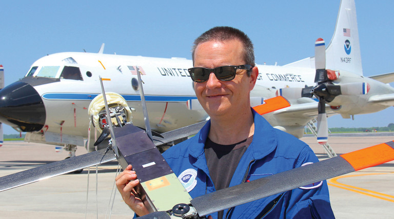 Joe Cione holding a drone and standing in front of a plane