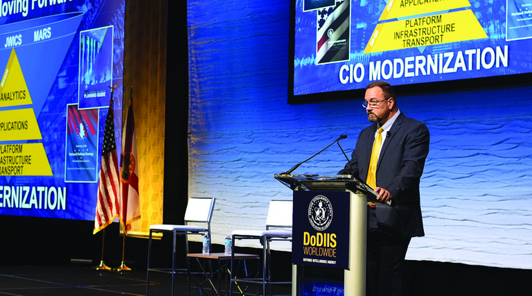 Man at podium with slides of pyramids with words