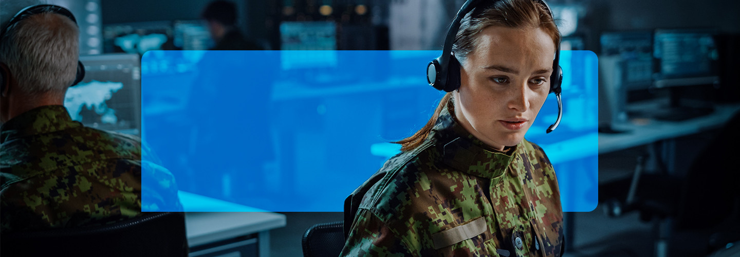 Woman with headset on, in a room with other people working on computers.