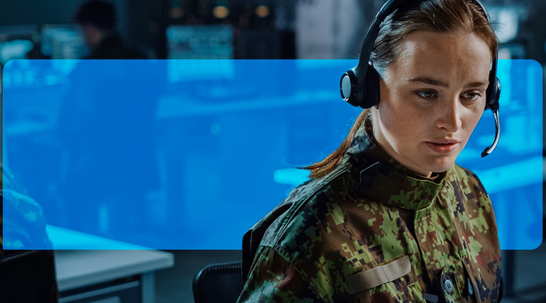 Woman with headset on, in a room with other people working on computers.