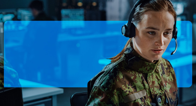 Woman with headset on, in a room with other people working on computers.